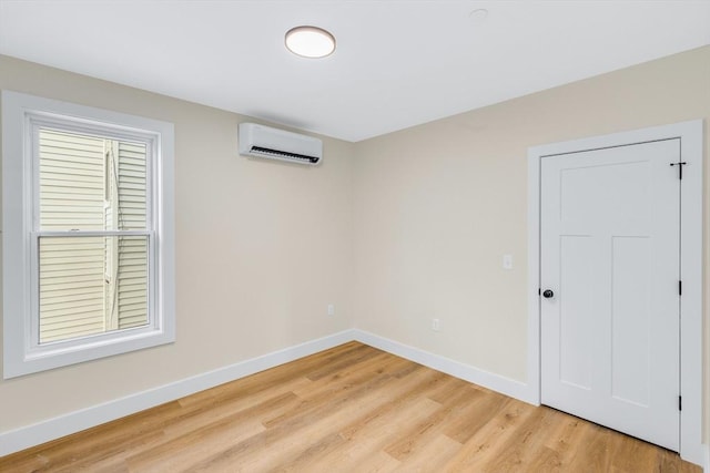 unfurnished room with light wood-style floors, baseboards, and a wall mounted AC