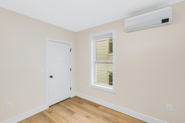 spare room with light wood-type flooring, a wall unit AC, and baseboards