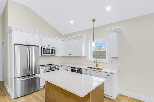 kitchen with white cabinets, vaulted ceiling, stainless steel appliances, light countertops, and a sink