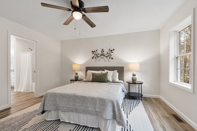 bedroom with multiple windows, ceiling fan, ensuite bathroom, and light wood-type flooring