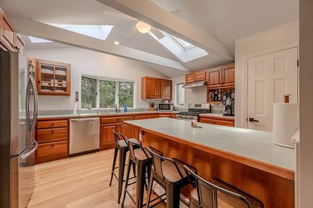 9 Brucewood, Acton, MA 01720 - kitchen with a breakfast bar area, appliances with stainless steel finishes, lofted ceiling with skylight, under cabinet range hood, and light wood-style flooring