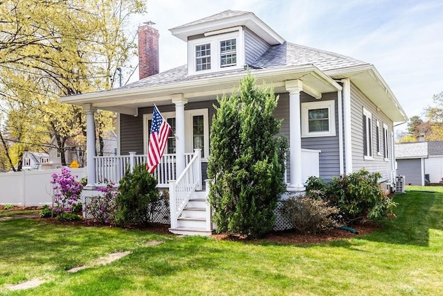 bungalow featuring covered porch, a chimney, a shingled roof, and a front yard