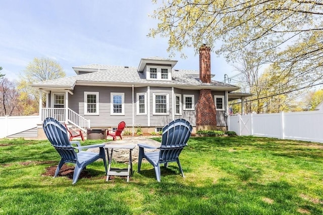 back of property with a lawn, a chimney, a fenced backyard, and roof with shingles