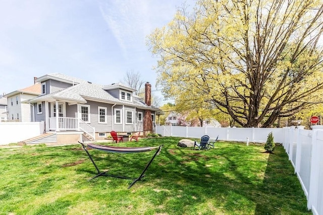rear view of property with a fenced backyard, a yard, and a chimney