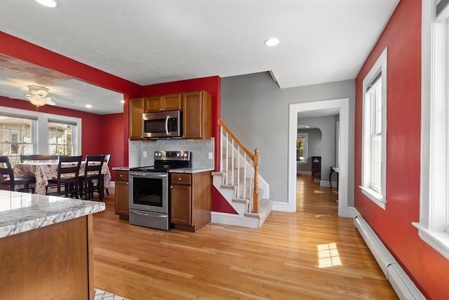 kitchen with brown cabinets, appliances with stainless steel finishes, baseboard heating, decorative backsplash, and light wood-type flooring