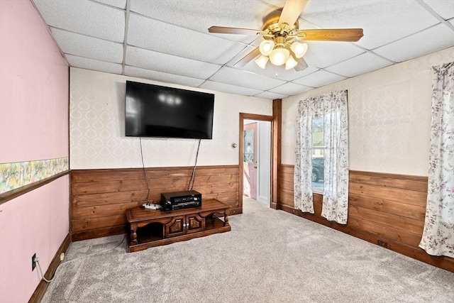 carpeted living room featuring ceiling fan, a paneled ceiling, and wood walls