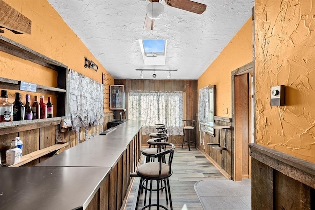 bar featuring ceiling fan, track lighting, a textured ceiling, light wood-type flooring, and wood walls