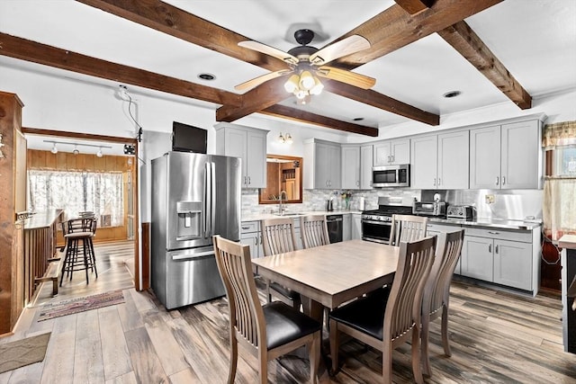 kitchen with gray cabinets, beam ceiling, stainless steel appliances, tasteful backsplash, and light wood-type flooring