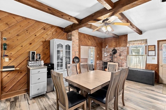 dining area featuring wooden walls, beam ceiling, light hardwood / wood-style flooring, and a wood stove