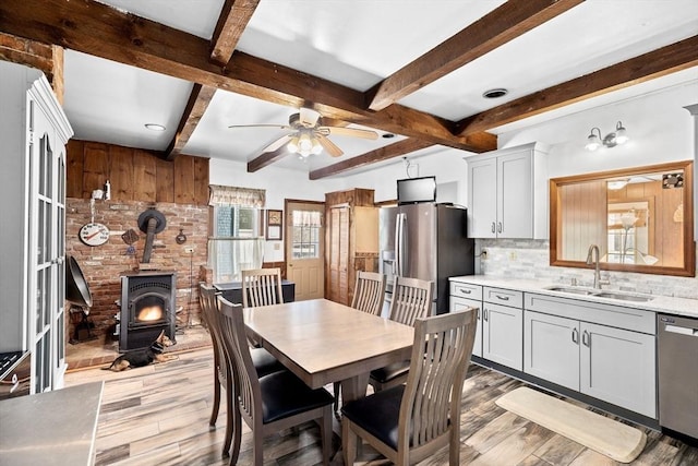 dining area with beamed ceiling, sink, a wood stove, ceiling fan, and light wood-type flooring