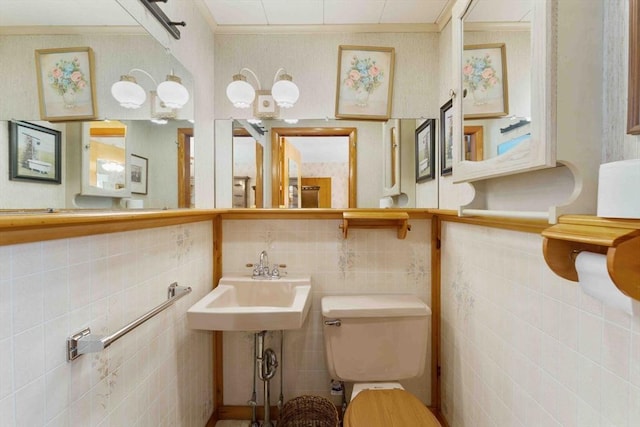 half bath with ornamental molding, a sink, tile walls, and toilet