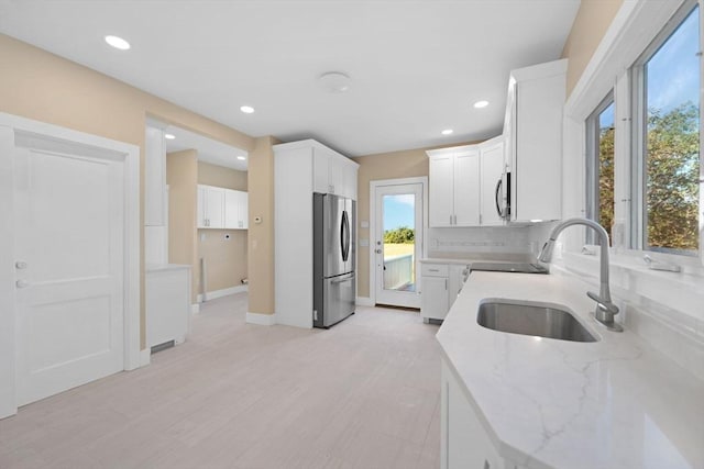 kitchen with tasteful backsplash, appliances with stainless steel finishes, light stone counters, white cabinetry, and a sink