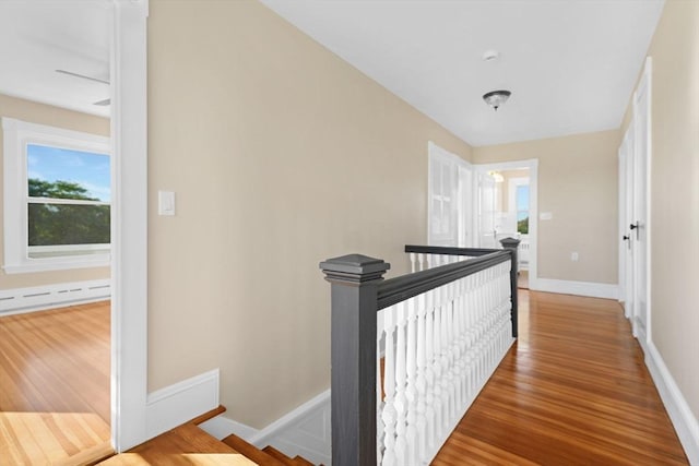 hallway with a baseboard radiator, wood finished floors, an upstairs landing, and baseboards