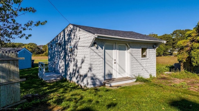 back of property with concrete block siding, a lawn, and an outbuilding