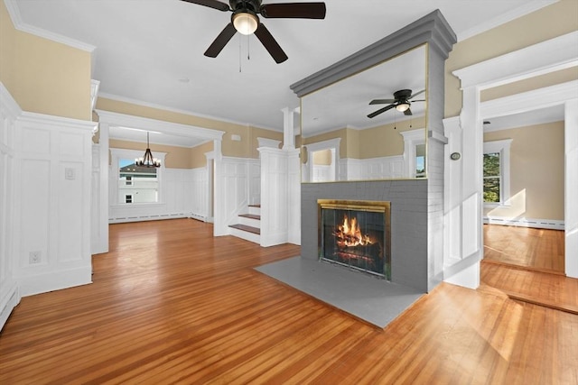 unfurnished living room featuring a baseboard radiator, wood finished floors, ornamental molding, wainscoting, and a brick fireplace