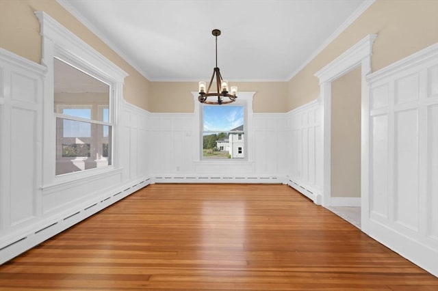 unfurnished dining area featuring a decorative wall, a baseboard heating unit, light wood-type flooring, an inviting chandelier, and crown molding