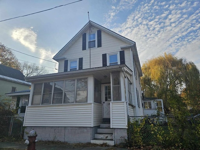 view of front facade featuring entry steps, fence, and a sunroom