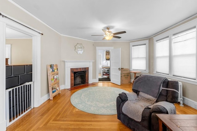 living room featuring ceiling fan, crown molding, light parquet floors, and a fireplace