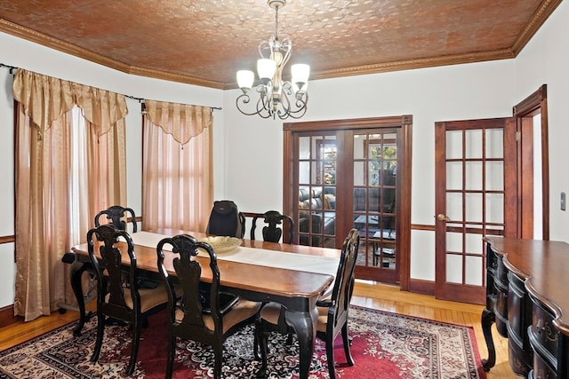 dining space with hardwood / wood-style flooring, a notable chandelier, ornamental molding, and french doors