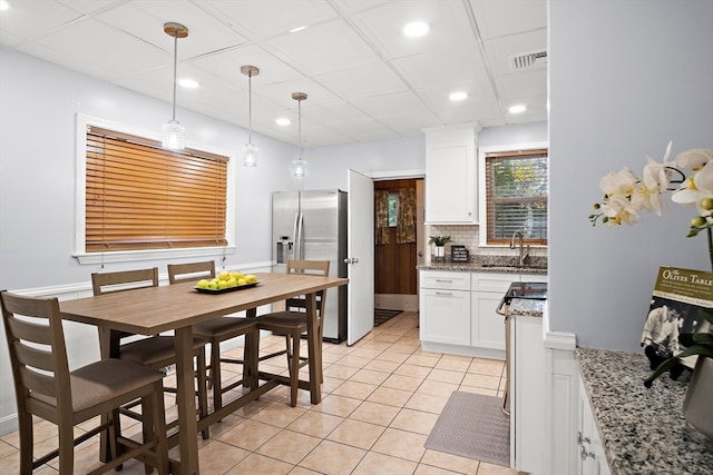 kitchen featuring light stone counters, white cabinets, stainless steel fridge with ice dispenser, hanging light fixtures, and light tile patterned flooring