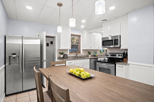 kitchen with sink, stainless steel appliances, white cabinets, decorative light fixtures, and light tile patterned flooring