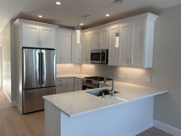 kitchen with kitchen peninsula, white cabinets, decorative light fixtures, and appliances with stainless steel finishes