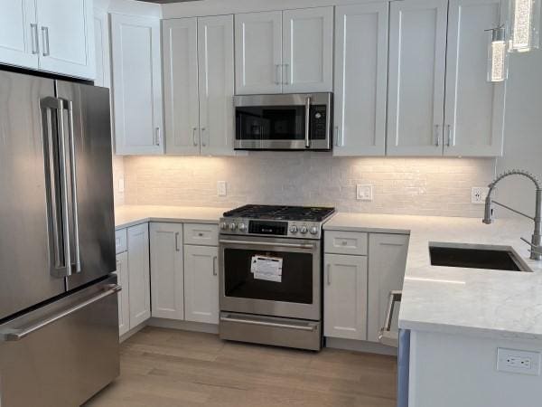 kitchen featuring light hardwood / wood-style floors, tasteful backsplash, white cabinetry, sink, and stainless steel appliances