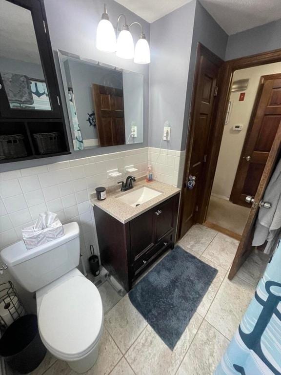 bathroom with toilet, tile patterned flooring, tile walls, and vanity