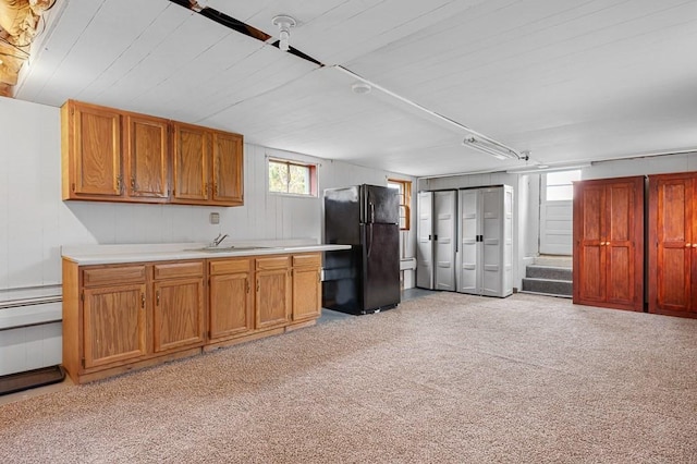 kitchen featuring light colored carpet, a sink, light countertops, freestanding refrigerator, and brown cabinets