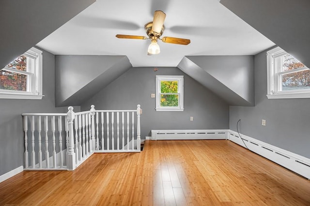 additional living space with vaulted ceiling, a baseboard radiator, light wood-style flooring, and baseboards