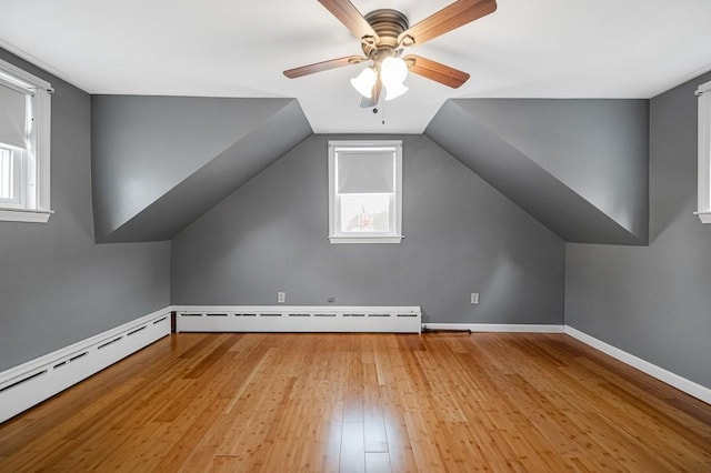 bonus room with a baseboard heating unit, light wood-type flooring, a ceiling fan, and baseboards