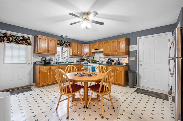 kitchen with dark countertops, under cabinet range hood, brown cabinets, and freestanding refrigerator