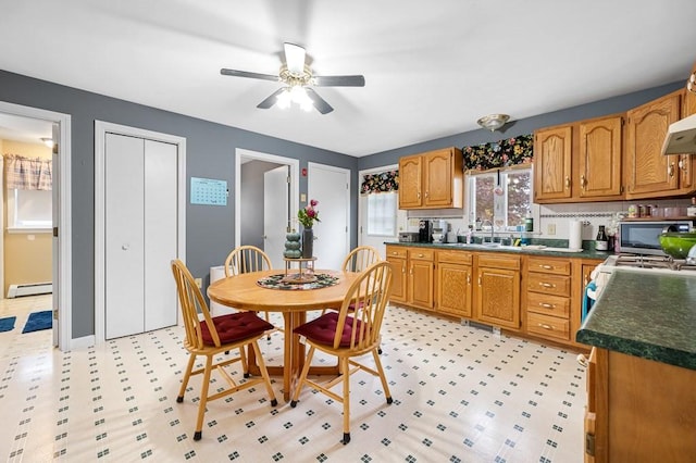 kitchen with white gas range oven, a ceiling fan, dark countertops, a baseboard radiator, and a sink