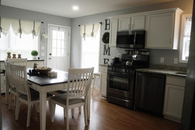 kitchen with black appliances, dark stone countertops, dark wood finished floors, and white cabinets