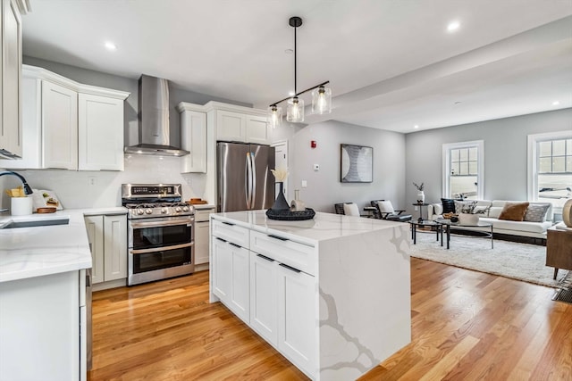 kitchen featuring appliances with stainless steel finishes, wall chimney exhaust hood, light wood-type flooring, and white cabinets