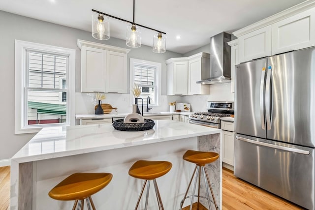 kitchen with wall chimney exhaust hood, a center island, appliances with stainless steel finishes, and pendant lighting