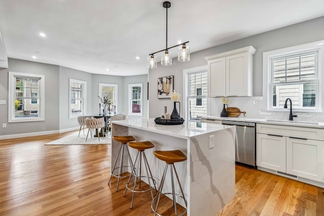 kitchen with light hardwood / wood-style floors, sink, white cabinets, a kitchen island, and light stone countertops