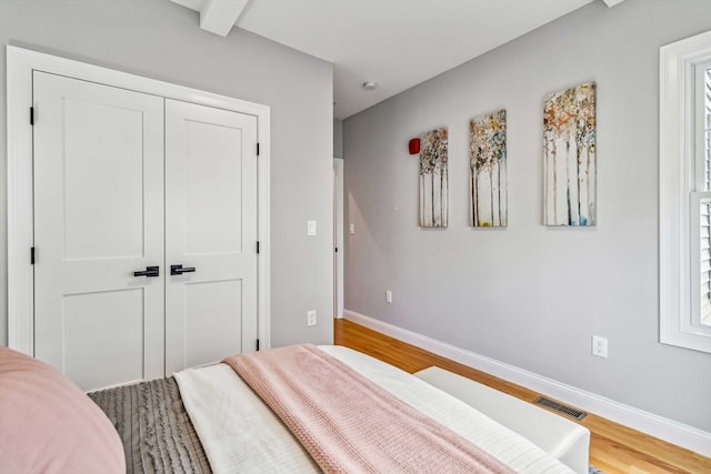 bedroom with beam ceiling, multiple windows, a closet, and hardwood / wood-style flooring