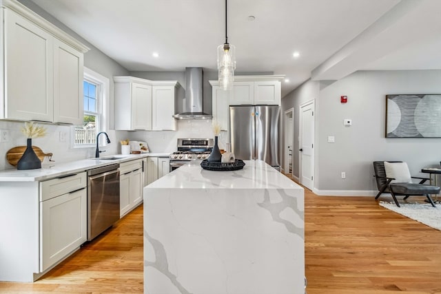 kitchen featuring appliances with stainless steel finishes, light hardwood / wood-style floors, a center island, sink, and wall chimney range hood