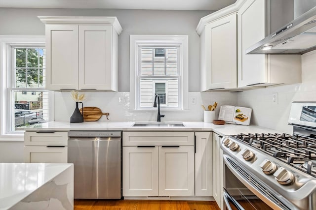 kitchen featuring stainless steel appliances, sink, wall chimney range hood, and white cabinetry