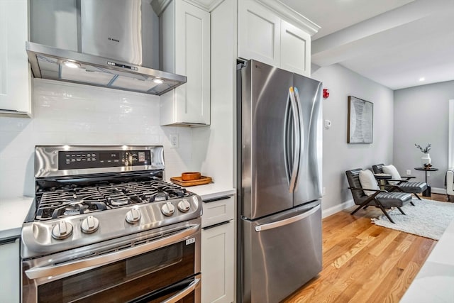 kitchen featuring light hardwood / wood-style flooring, backsplash, wall chimney range hood, white cabinetry, and appliances with stainless steel finishes