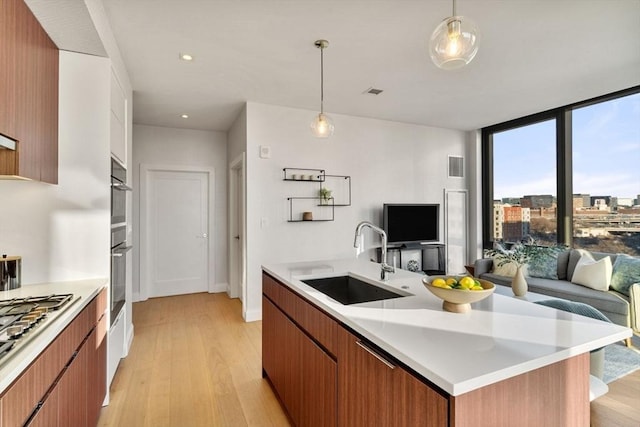 kitchen with light wood-type flooring, a sink, open floor plan, stainless steel appliances, and light countertops