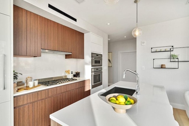 kitchen with a sink, stainless steel appliances, light countertops, under cabinet range hood, and modern cabinets