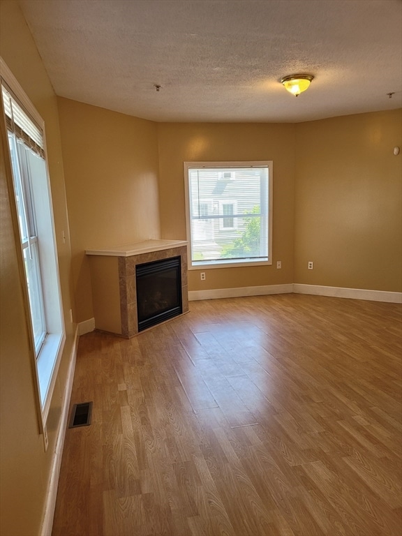 unfurnished living room featuring a tile fireplace, a textured ceiling, and light hardwood / wood-style flooring