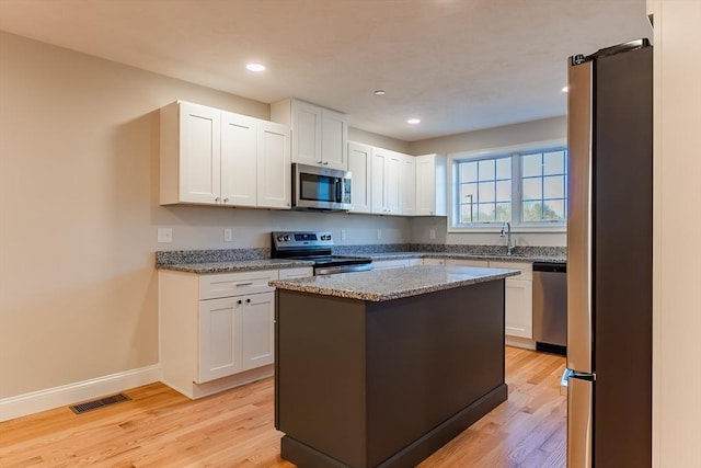 kitchen featuring white cabinets, light hardwood / wood-style flooring, light stone countertops, appliances with stainless steel finishes, and a kitchen island