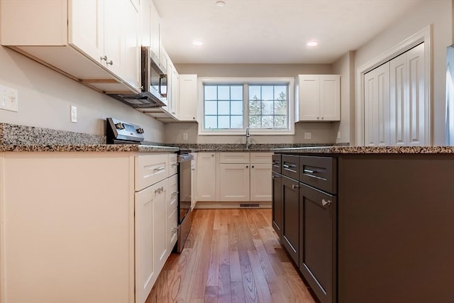 kitchen featuring sink, light stone countertops, light wood-type flooring, appliances with stainless steel finishes, and white cabinetry