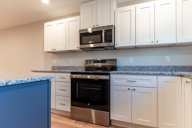 kitchen with white cabinets, light stone counters, stainless steel appliances, and light hardwood / wood-style flooring