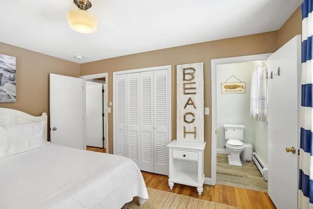 bedroom with ensuite bath, a baseboard heating unit, light hardwood / wood-style floors, and a closet