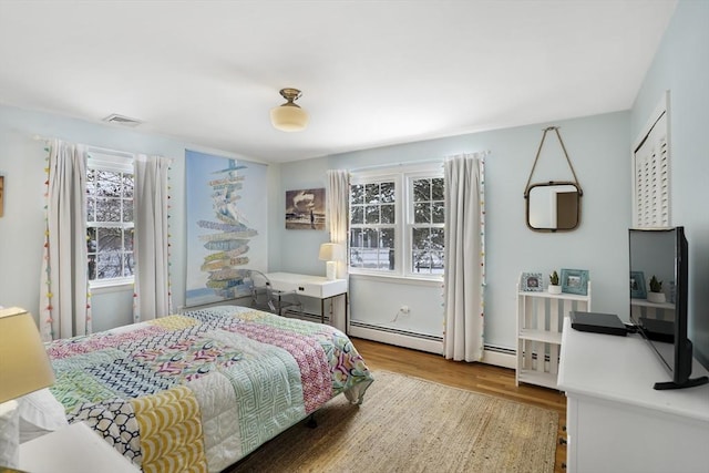 bedroom featuring a baseboard radiator, light hardwood / wood-style floors, and multiple windows