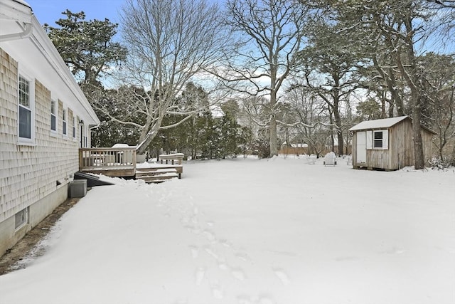 yard layered in snow featuring a wooden deck and a shed